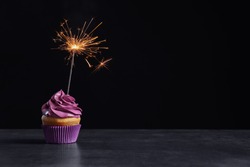 Delicious birthday cupcake with sparkler on table against black background