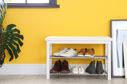 Collection of stylish shoes on rack storage near color wall in room