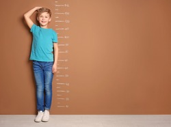 Little boy measuring his height near color wall