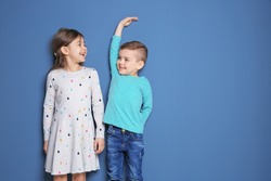 Little girl and boy measuring their height on color background