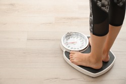 Woman measuring her weight using scales on wooden floor. Healthy diet
