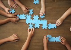 Top view of little children playing puzzle together at table, focus on hands. Unity concept