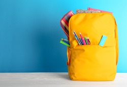 Backpack with different colorful stationery on table. Back to school