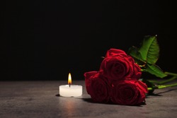 Beautiful red roses and candle on table against black background. Funeral symbol