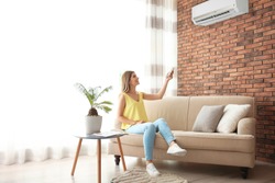 Woman operating air conditioner while sitting on sofa at home