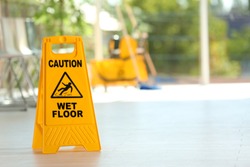 Safety sign with phrase Caution wet floor and blurred mop bucket on background. Cleaning service