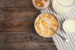 Flat lay composition with healthy cornflakes and milk in bowl on wooden table. Space for text