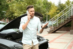 Man talking on phone near broken car outdoors