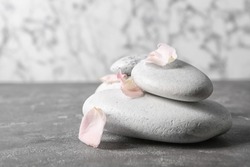 Spa stones and flower petals on grey table. Space for text