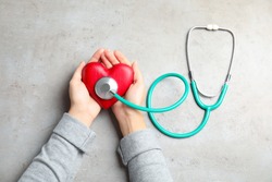 Woman holding red heart and stethoscope on gray background, top view. Cardiology concept