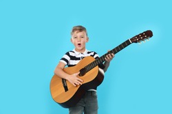 Portrait of little boy playing guitar on color background