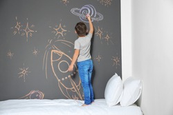Little child drawing rocket with chalk on wall in bedroom