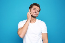 Young man scratching face on color background. Annoying itch