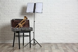 Trumpet, chair, case and note stand with music sheets near brick wall. Space for text