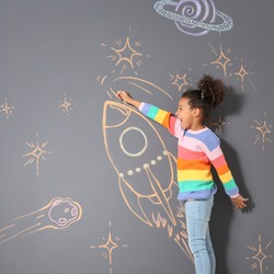 African-American child playing with chalk rocket drawing on grey background