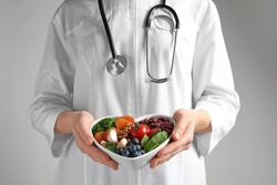 Doctor holding bowl with products for heart-healthy diet on color background, closeup