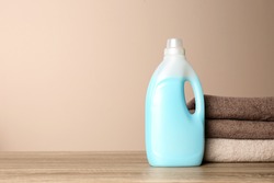 Bottle of detergent and clean towels on table against color background, space for text. Laundry day