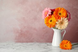 Bouquet of beautiful bright gerbera flowers in vase on marble table against color background