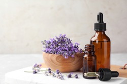 Bottles with natural essential oil and bowl of lavender flowers on table against light background. Space for text