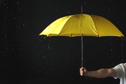 Man holding yellow umbrella under rain against black background, closeup