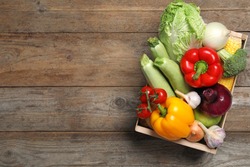 Fresh vegetables in crate on wooden background, top view. Space for text
