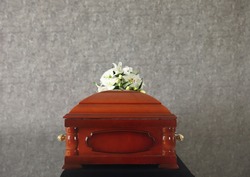 Wooden funeral casket with white lilies at grey wall
