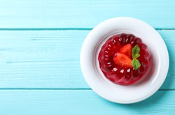 Delicious red jelly with strawberry and mint on light blue wooden table, top view. Space for text
