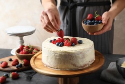 Woman decorating delicious homemade cake with fresh berries at table indoors, closeup