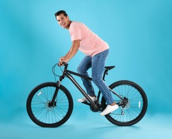 Handsome young man with modern bicycle on light blue background
