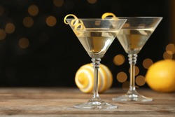 Glasses of Lemon Drop Martini cocktail with zest on wooden table against blurred background. Space for text