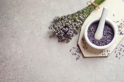 Top view of mortar and pestle with lavender flowers on grey stone background, space for text. Natural cosmetic