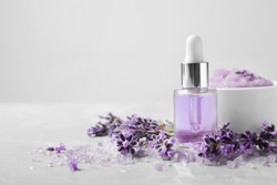 Natural cosmetic oil, bath salt, scrub and lavender flowers on grey marble table, space for text