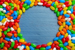 Frame made of colorful jelly beans on blue wooden background, flat lay. Space for text