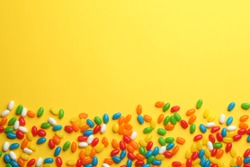 Tasty colorful jelly beans on yellow background, flat lay. Space for text