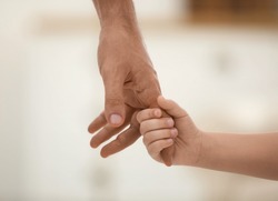 Father holding hands with his child indoors, closeup. Happy family