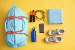 Gym bag, smartphone and sports equipment on yellow background, flat lay