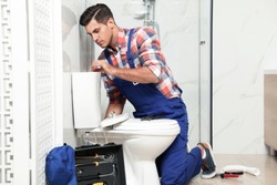 Professional plumber working with toilet bowl in bathroom