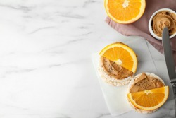 Puffed rice cakes with peanut butter and orange on white marble table, flat lay. Space for text