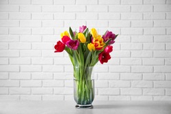 Beautiful spring tulips in vase on table near white brick wall