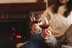 Lovely couple with glasses of wine resting near fireplace at home, closeup. Winter vacation