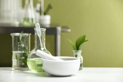 Mortar with pestle and natural ingredients on white table in cosmetic laboratory