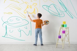 Little child drawing scribbles on white wall indoors