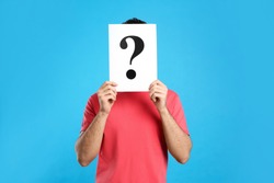 Young man with question mark sign on light blue background