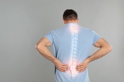 Man suffering from pain in spine on grey background