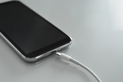 Mobile phone and charging cable on white table, closeup