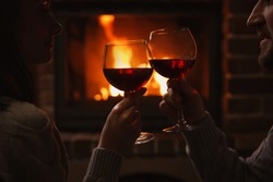 Couple with glasses of red wine near burning fireplace, closeup