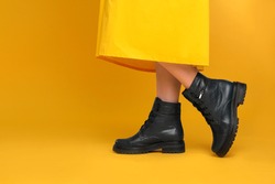Woman wearing stylish boots on yellow background, closeup. Space for text
