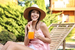 Young woman with refreshing drink resting in deck chair outdoors