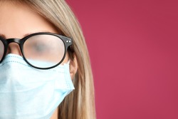 Woman with foggy glasses caused by wearing disposable mask on pink background, space for text. Protective measure during coronavirus pandemic