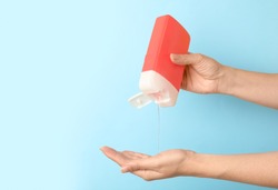 Woman pouring personal hygiene product on hand against light blue background, closeup